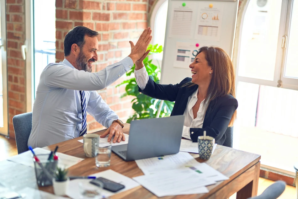 Two business professionals celebrating success with a high five in a modern office.