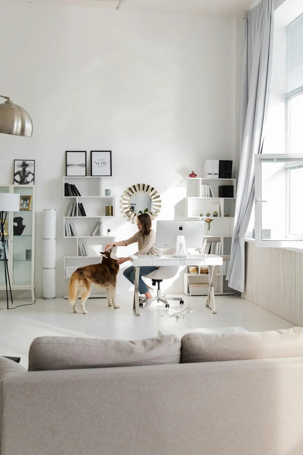 Woman working in a bright modern home office petting her dog beside the desk.